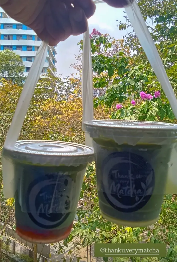 Two matcha drinks in takeaway bags held up outdoors