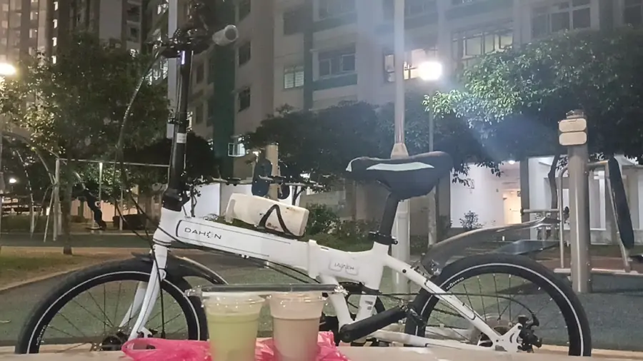 Two matcha drinks on a bench beside a bicycle at night